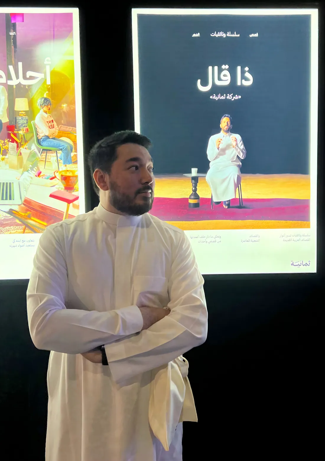 Jemeel Alturkustani in a white thobe, standing in front of illuminated posters for the documentary series He Said
