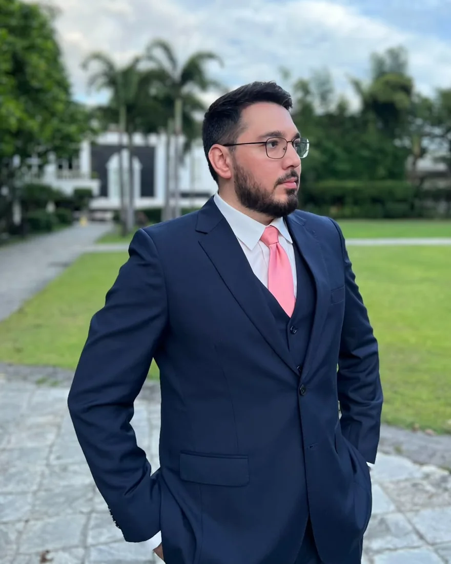 Jemeel Alturkustani in a navy three-piece suit and pink tie, standing outdoors